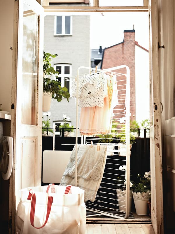 Una finestra aperta su un balcone dove c'è uno stendino per biancheria con alcuni indumenti stesi e mossi dal vento. Si vedono anche una borsa e alcuni vasi SAMVERKA a lato del balcone.