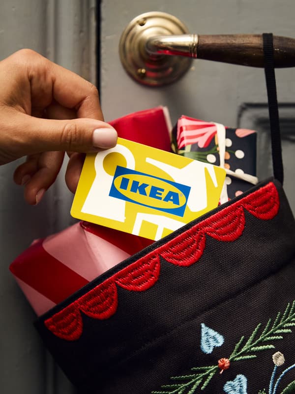 Una gift card IKEA gialla, all'interno di una calza di Natale appesa alla maniglia di una porta e piena di pacchi regalo.