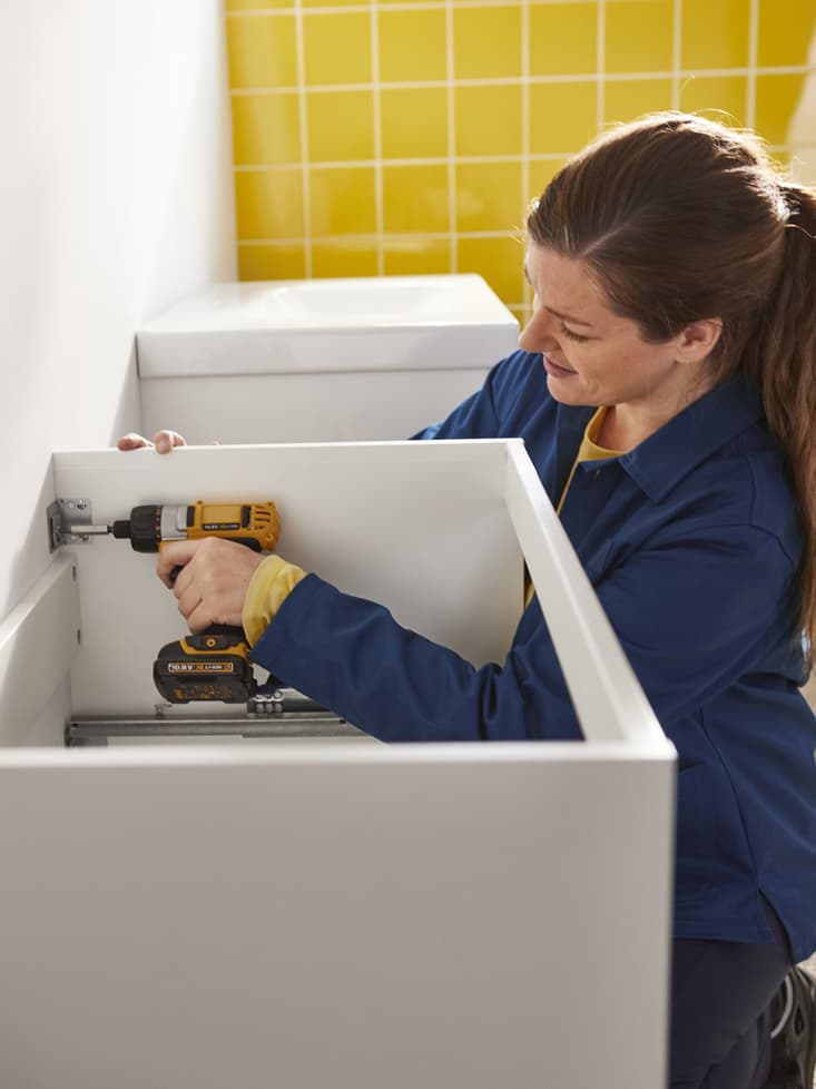 Una giovane donna che fissa al muro un mobile da cucina bianco IKEA.