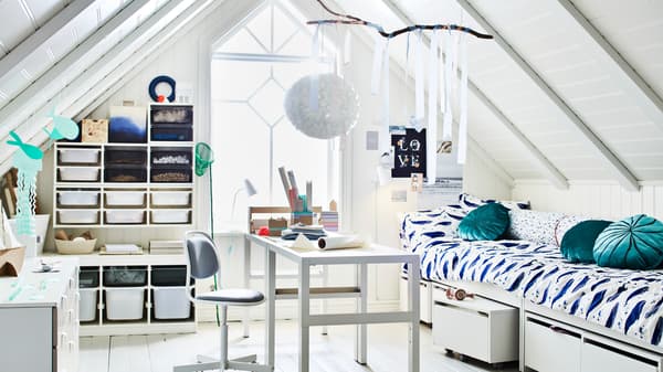 Una habitación con techo abuhardillado y un amplio ventanal. En medio de la habitación hay dos escritorios PÅHL, cerca de dos camas y varias soluciones de almacenaje TROFAST.