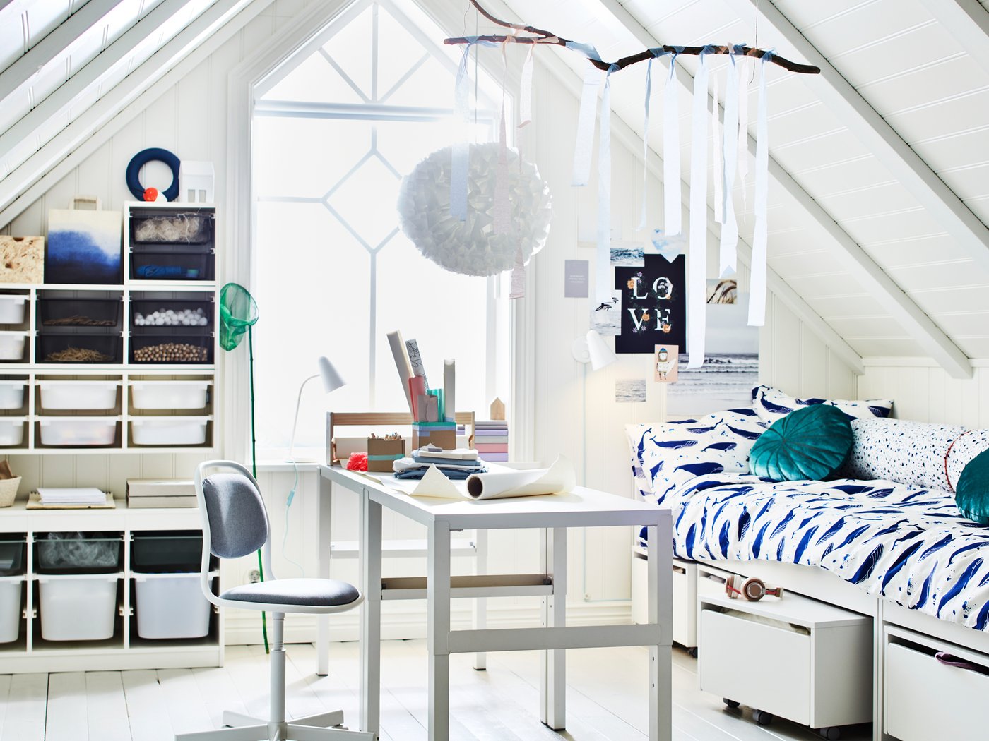 Una habitación con techo inclinado y un amplio ventanal. En medio de la habitación hay dos escritorios PÅHL, cerca de dos camas y varias soluciones de almacenaje TROFAST.