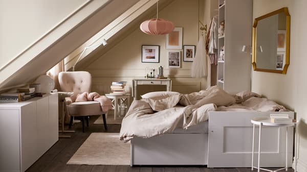 Una habitación con un diván-cama abierto y ropa de campa beige/gris claro, almacenamiento diverso, un sillón beige y una lámpara de techo rosa.