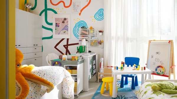 Una habitación infantil compartida donde algunos muebles MAMMUT infantiles se encuentran cerca de un escritorio MICKE blanco y un carrito ÖVNING.
