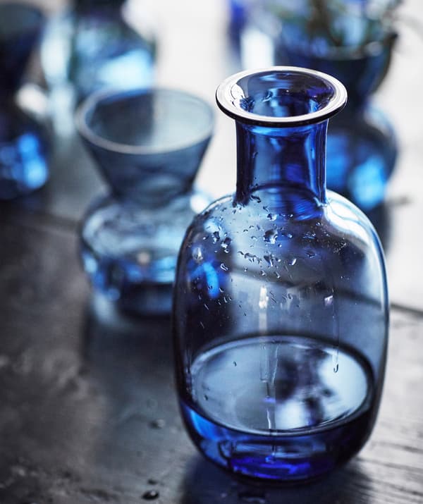 Una jarra de vidrio azul y jarrones azules pequeños encima de una mesa de madera oscura.