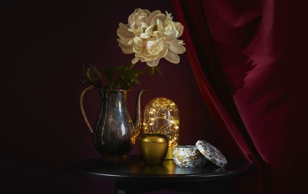Una lampada e decorazioni color oro su un tavolino rotondo contro uno sfondo rosso scuro - IKEA