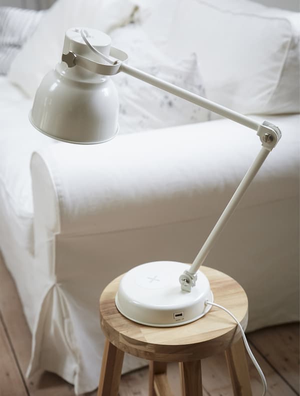 Una lampada su uno sgabello di legno di fianco a un divano bianco.