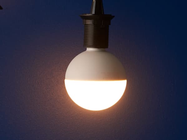 Una lampadina bianca su un attacco nero proietta la luce su uno sfondo blu.