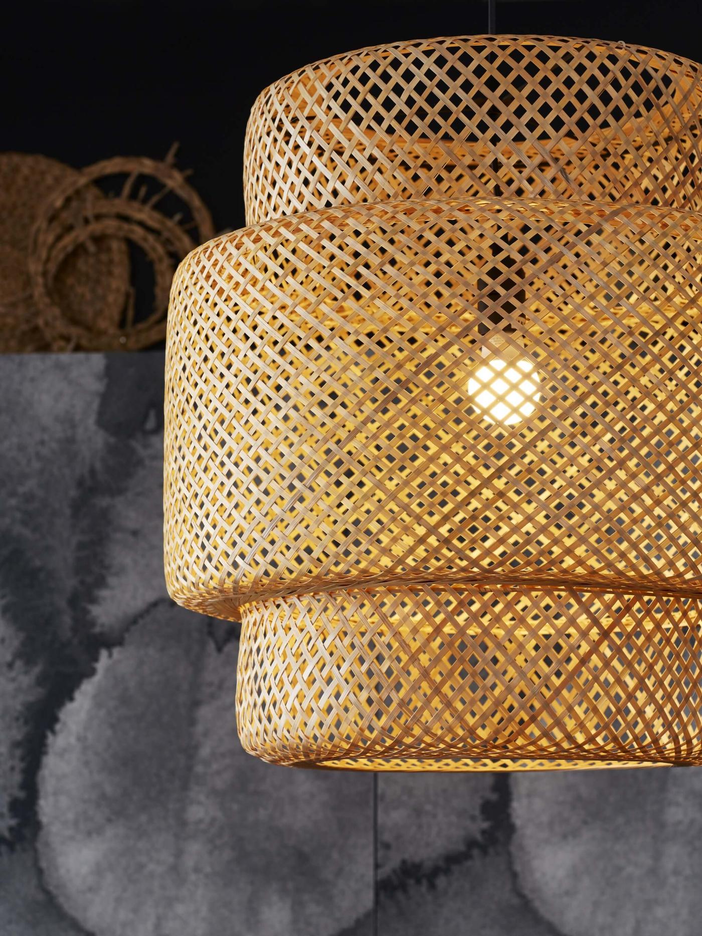 Una lámpara colgante de bambú SINNERLIG con la luz prendida.