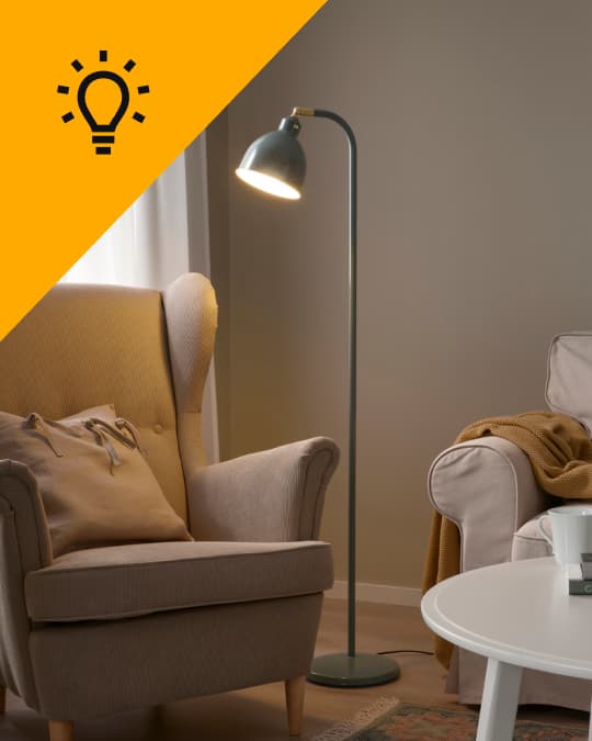 Una lámpara de pie iluminando la parte superior de un silón IKEA en un living.
