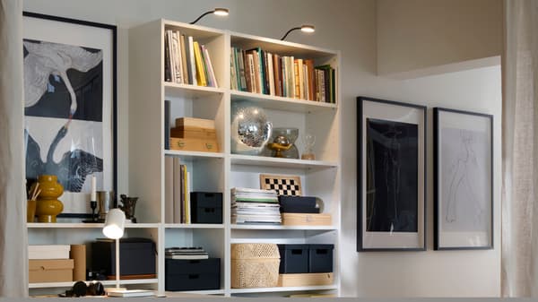 Una libreria BILLY illuminata, con all'interno libri ordinati, scatole, contenitori e altri oggetti decorativi.