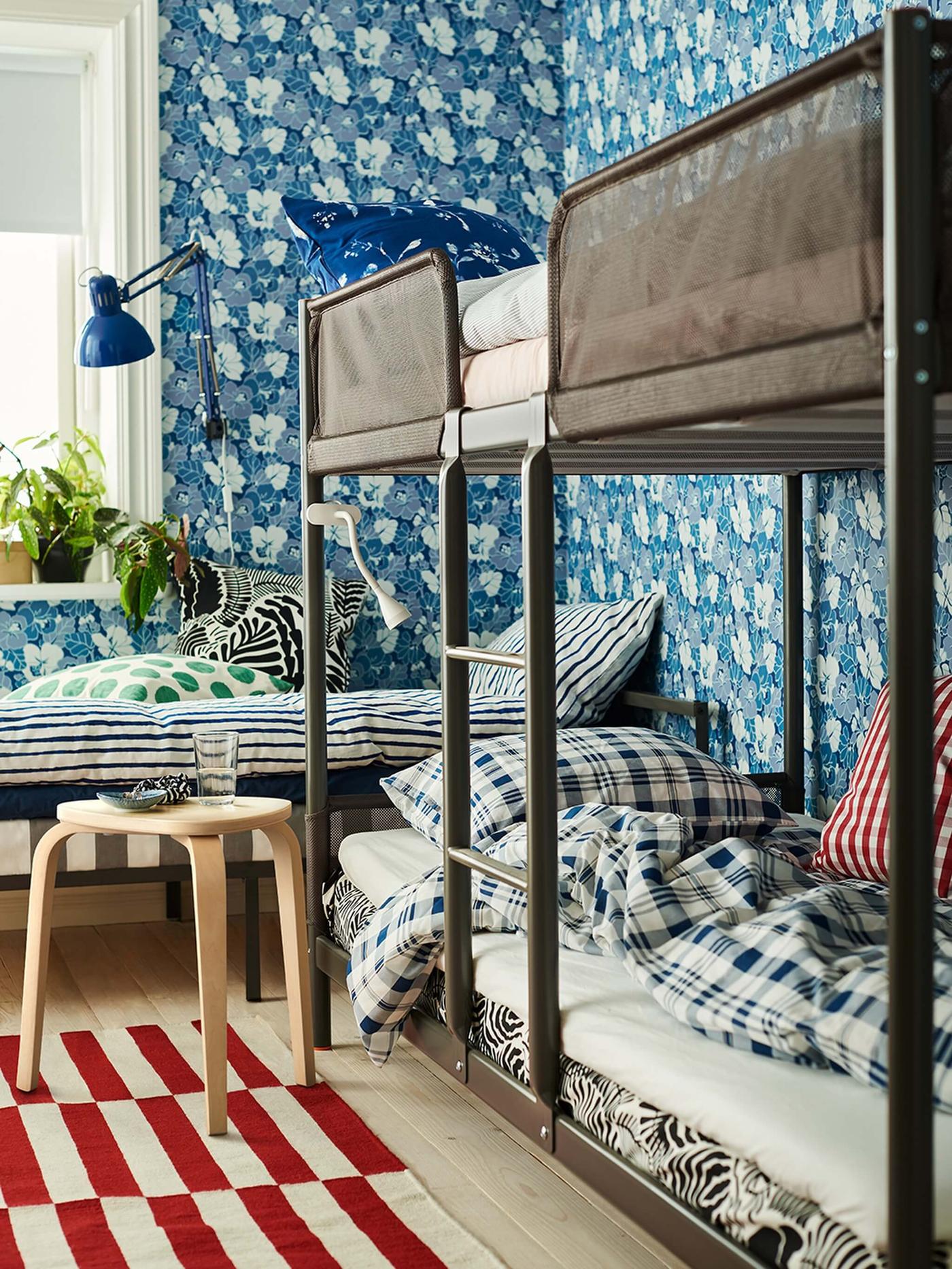 Una litera gris en una habitación infantil con un papel de pared floral en tonos azules.