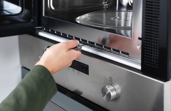 Una mà amb un tornavís col·locant un microones damunt d'un moble de cuina modular.