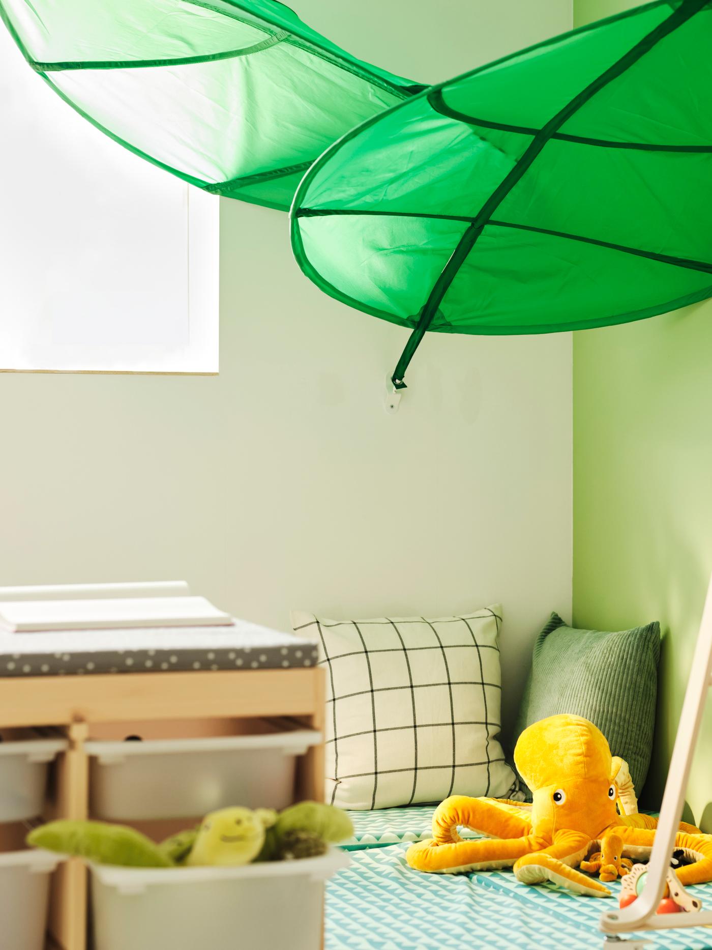 Una madre sentada bajo varios doseles LÖVA con un niño pequeño y dos bebés en un rincón acogedor.
