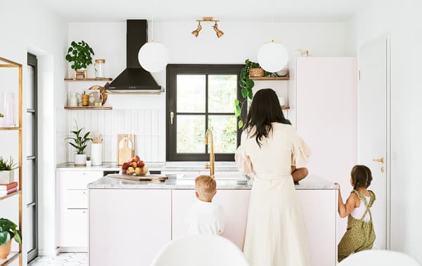 Una mamma e due bambini davanti all'isola di una cucina arredata con mobili rosa, piani di lavoro in marmo e finiture in ottone - IKEA
