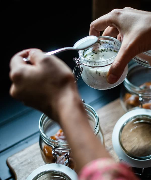Una mano che con un cucchiaino prende un po' di condimento a base di yogurt da un contenitore KORKEN.