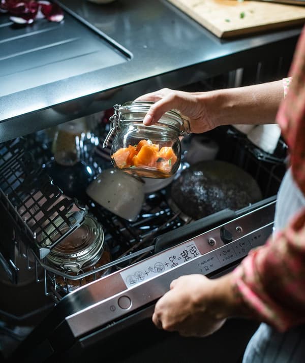 Una mano che inserisce in lavastoviglie un contenitore KORKEN con alimenti per fare la vasocottura.