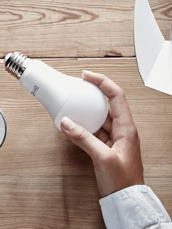 Una mano presionando el interruptor de una lámpara de mesa blanca sobre una mesa azul claro.