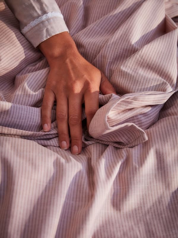 Una manta blanca y tres cuencos blancos sobre un reposapiés GAMLEHULT con libros guardados en su interior.