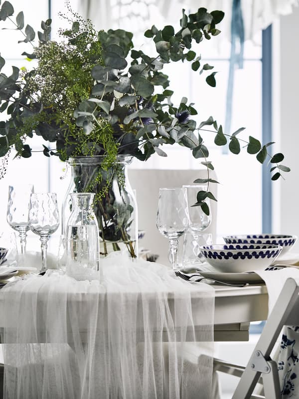 Una mesa de boda con un centro de mesa floral, sillas TERJE con respaldo de tela azul y un juego de comedor tradicional blanco. 