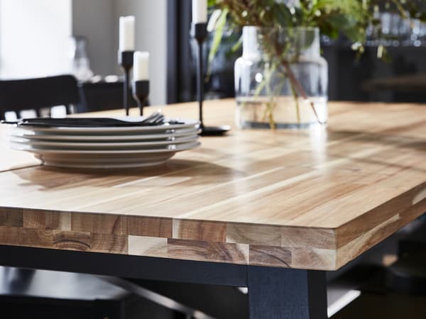 Una mesa de comedor con tablero de madera con un llamativo dibujo de vetas sobre la que hay una pila de platos, unos candelabros y un jarrón.