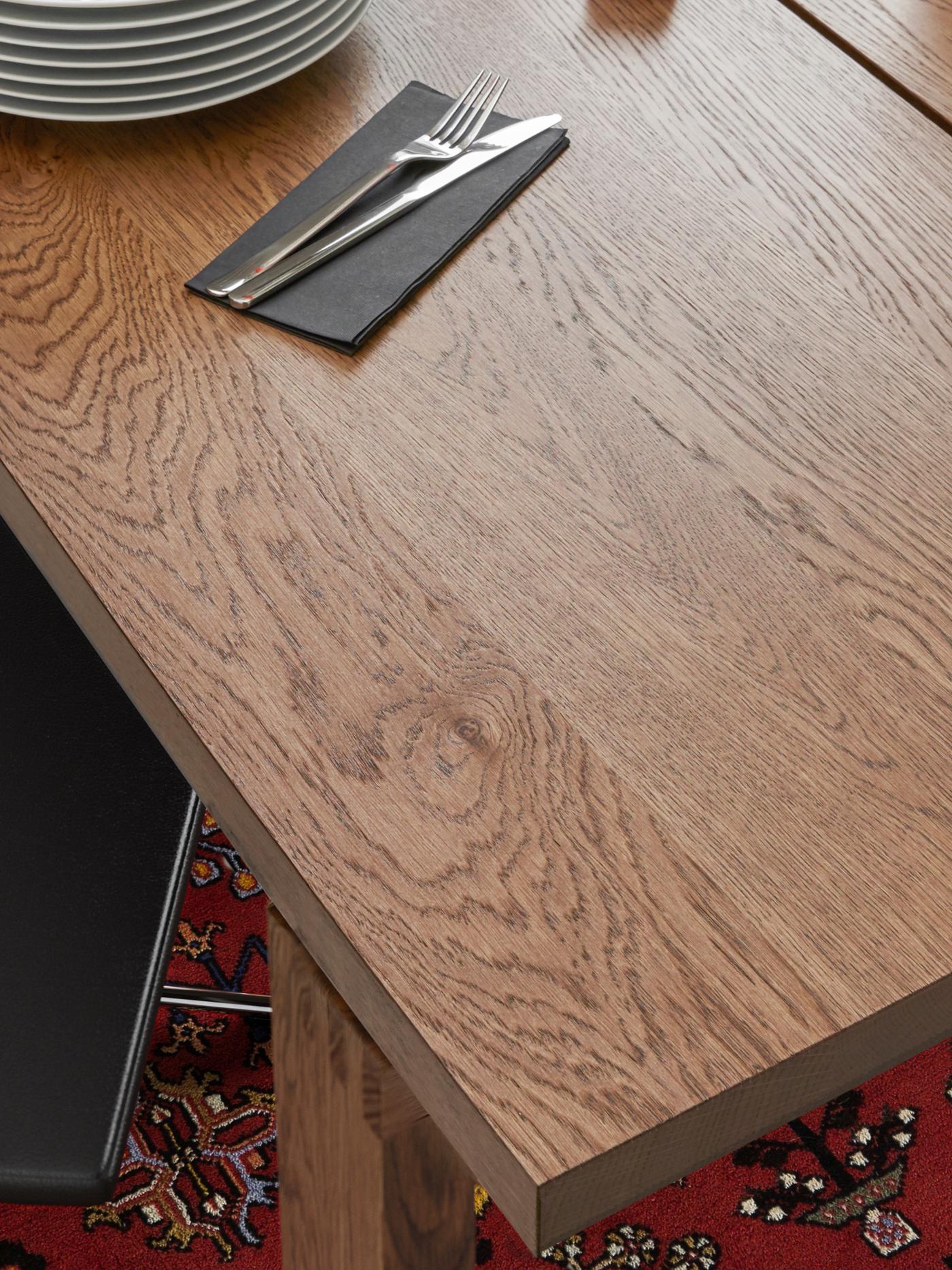 Una mesa de comedor MÖRBYLÅNGA sobre un tapete persa rojo. Sobre la mesa hay una pila de platos, una servilleta negra y un cuchillo y un tenedor.