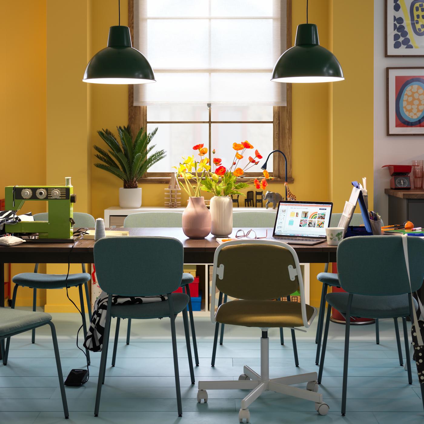 Una mesa extensible STRANDTORP de color marrón oscuro rodeada de varias sillas y organizada en varios puestos para llevar a cabo diversas actividades.