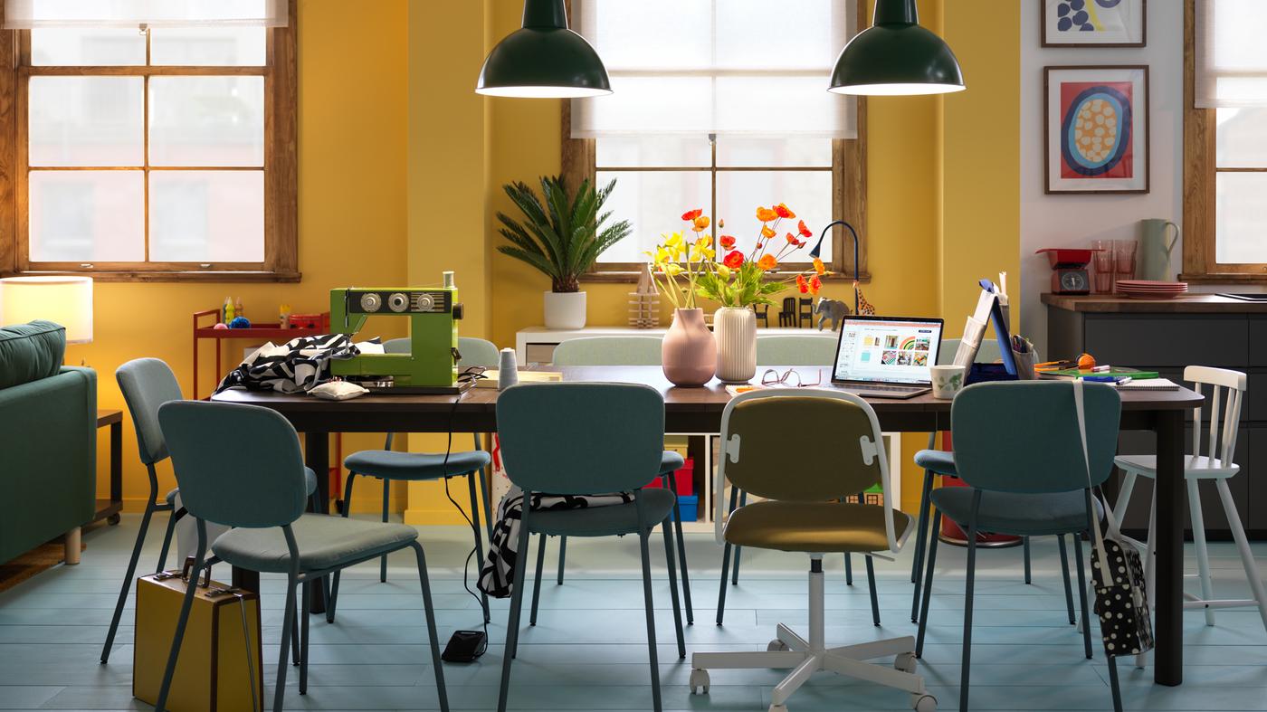 Una mesa extensible STRANDTORP de color marrón oscuro rodeada de varias sillas y organizada en varios puestos para llevar a cabo diversas actividades.