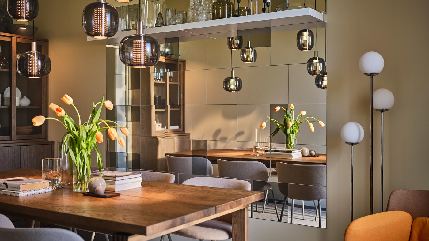 Una mesa larga MÖRBYLÅNGA en el centro de un comedor estrecho y sofisticado con una pared llena de espejos.