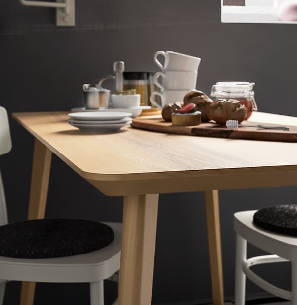 Una mesa LISABO de chapa de fresno con tazas de café y una tabla de cortar con un tarro de miel y algunos pasteles.