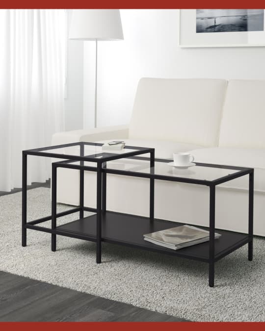 Una mesa nido de metal con cubierta de vidrio frente a un sofá blanco.