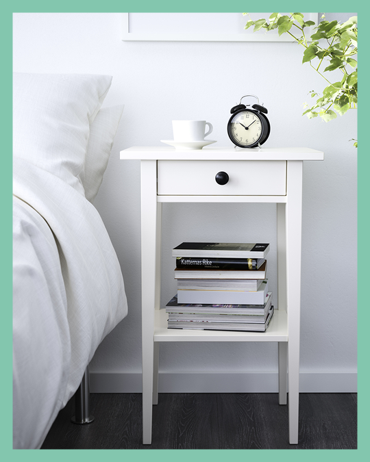 Una mesita de noche blanca con un cajón al costado de una cama.