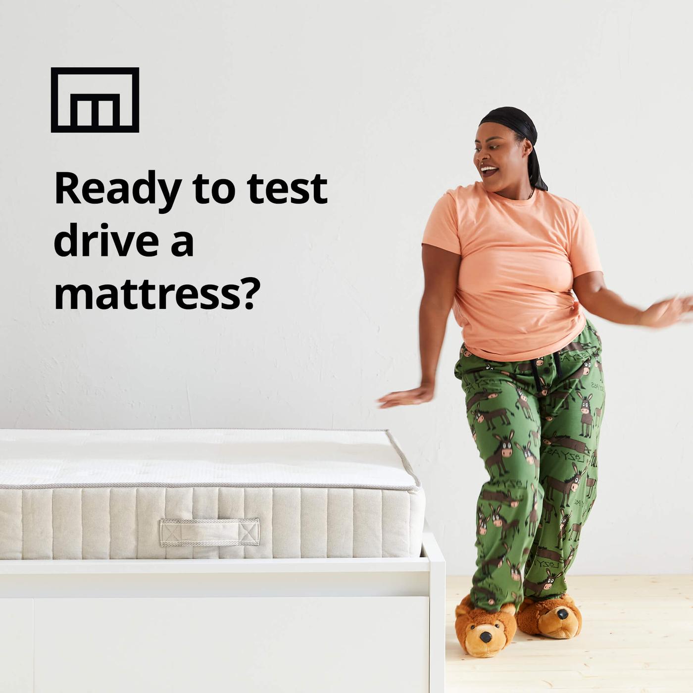Una mujer bailando en pijama junto a una cama y el símbolo de una caja de la tienda con el texto “¿Todo listo para poner a prueba el colchón?” sobre la imagen.