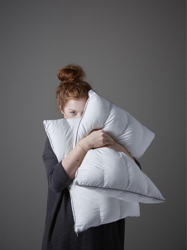 Una mujer colorina abrazando dos almohadas IKEA.