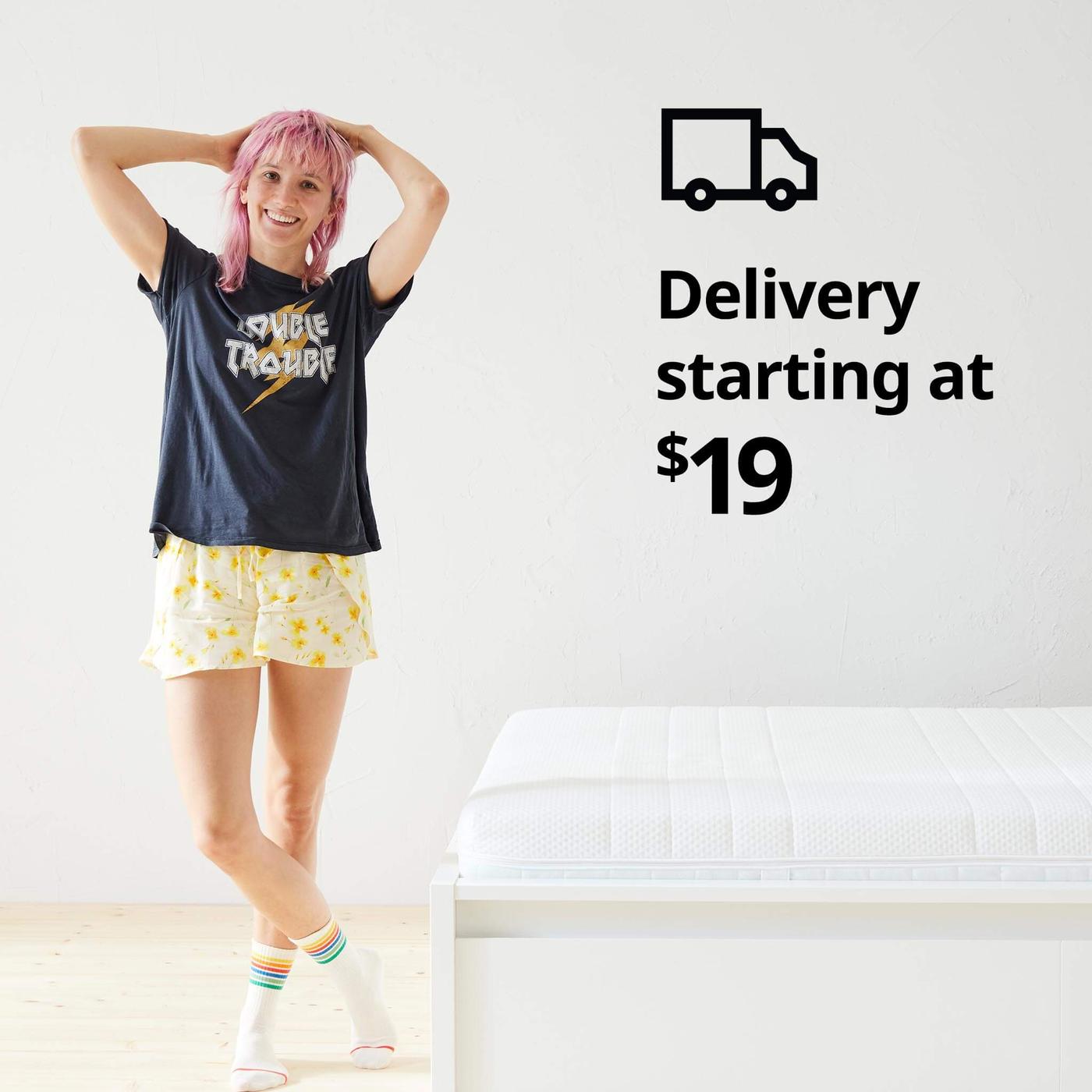 Una mujer de pie en pijama junto a una cama, el símbolo de un camión de reparto y el texto “Entregas a partir de $19” sobre la imagen.