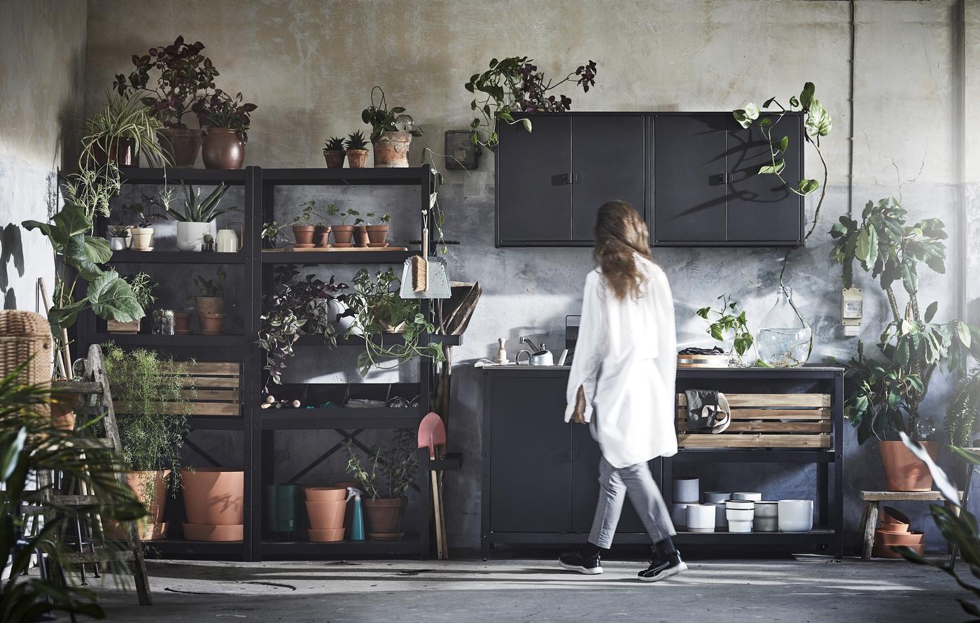Una mujer mirando una combinación de muebles negros con maceteros y plantas por todas partes.