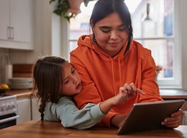 Una mujer mostrándole a una miña una tablet. La niña está a punto de tocar la pantalla con su dedo índice.