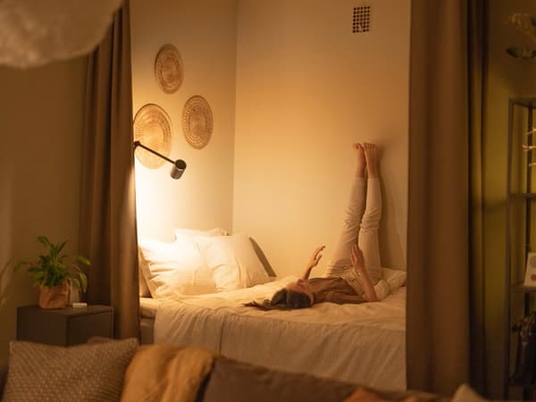 Una mujer recostada en una cama estirando las piernas en la pared.