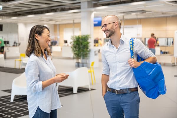 Una mujer sosteniendo una bolsa IKEA azul conversando con un hombre en un tienda IKEA.