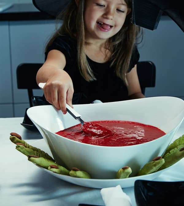 Una nena petita disfressada de bruixa que agafa una cullerada de sopa vermella.