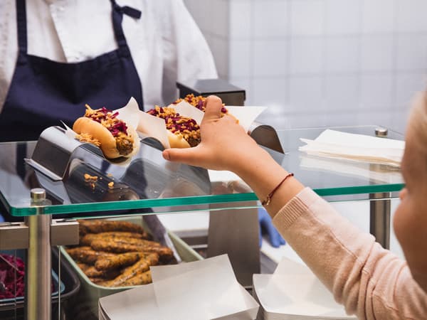 Una niña con un suéter rosa se acerca a recoger su hot dog vegetariano recién preparado del mostrador de una tienda IKEA.