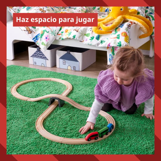 Una niña juega con un tren de madera IKEA sobre una alfombra infantil.