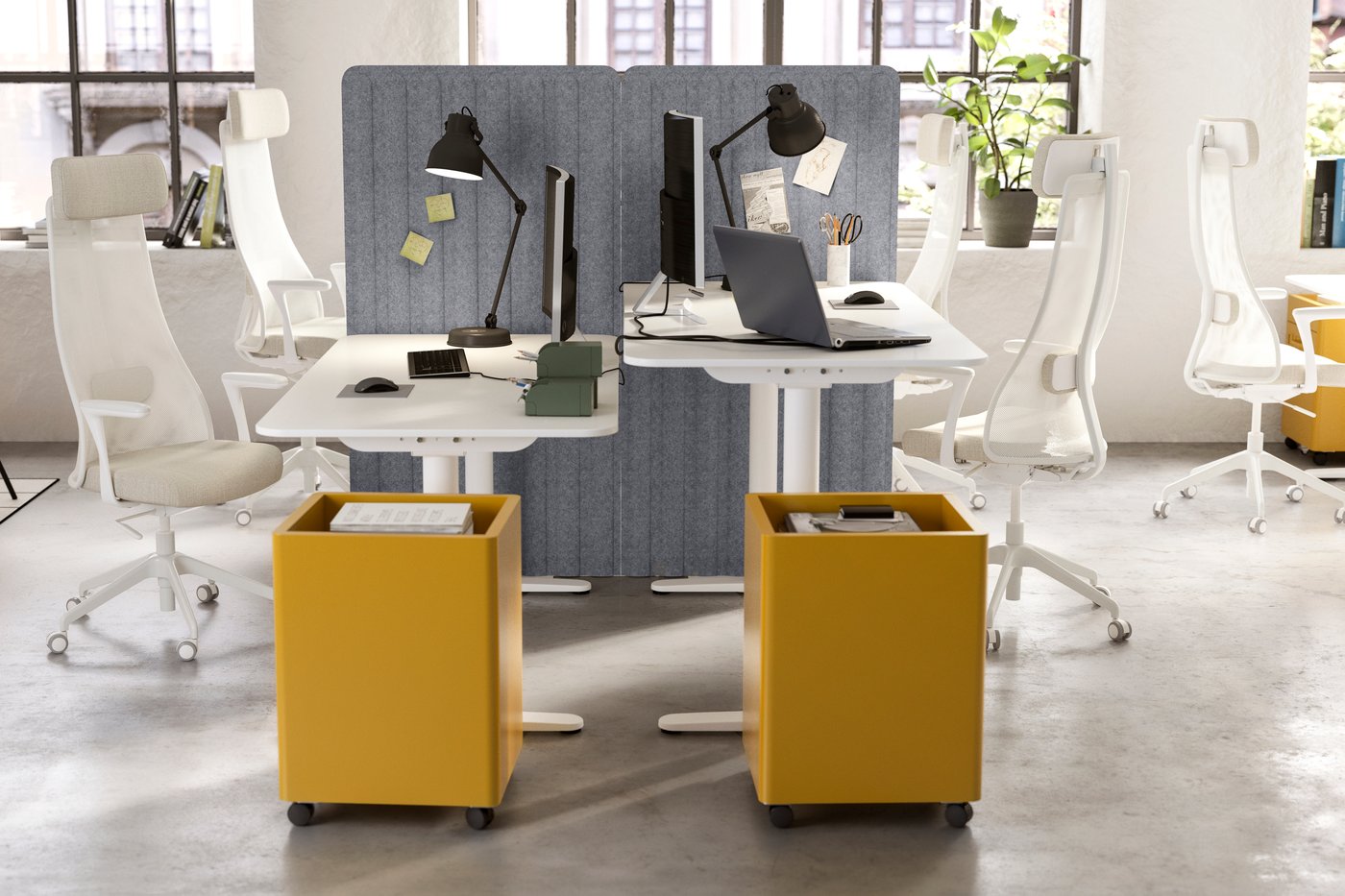Una oficina abierta con escritorios uno frente al otro y cada escritorio con cajoneras amarillas con ruedas.