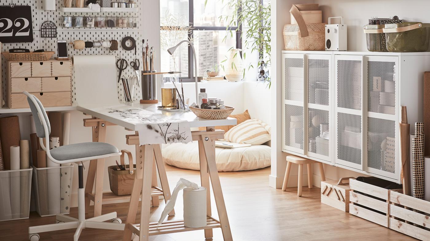 Una oficina doméstica con un escritorio blanco, una silla giratoria de color blanco y verde-amarillo y un tablero perforado blanco con materiales para hacer manualidades.