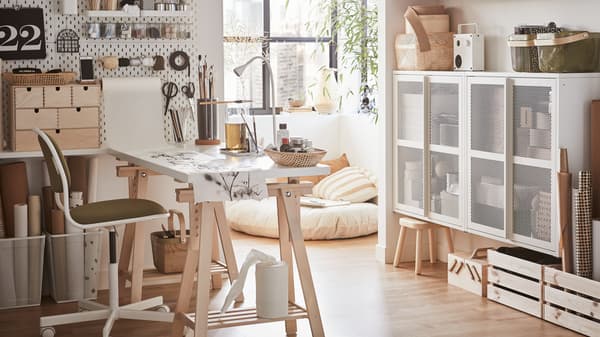 Una oficina en casa con un escritorio blanco, una silla giratoria de color blanco y verde-amarillo y un tablero perforado blanco con materiales para hacer manualidades.