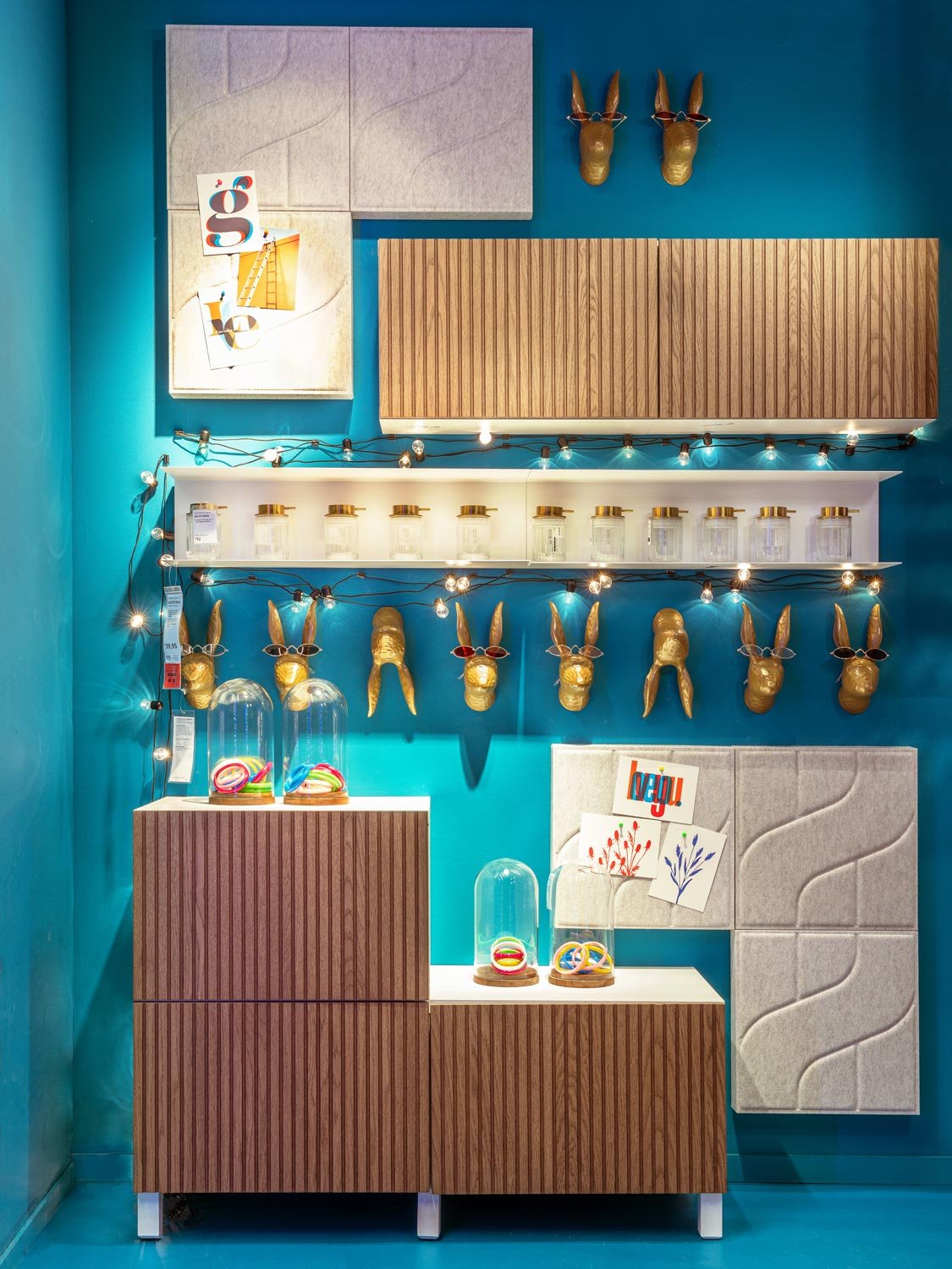 Una parete color ottanio con schermi acustici, ganci oro a forma di conilgio, attaccapanni e sotto, un mobile con ante cannettate.