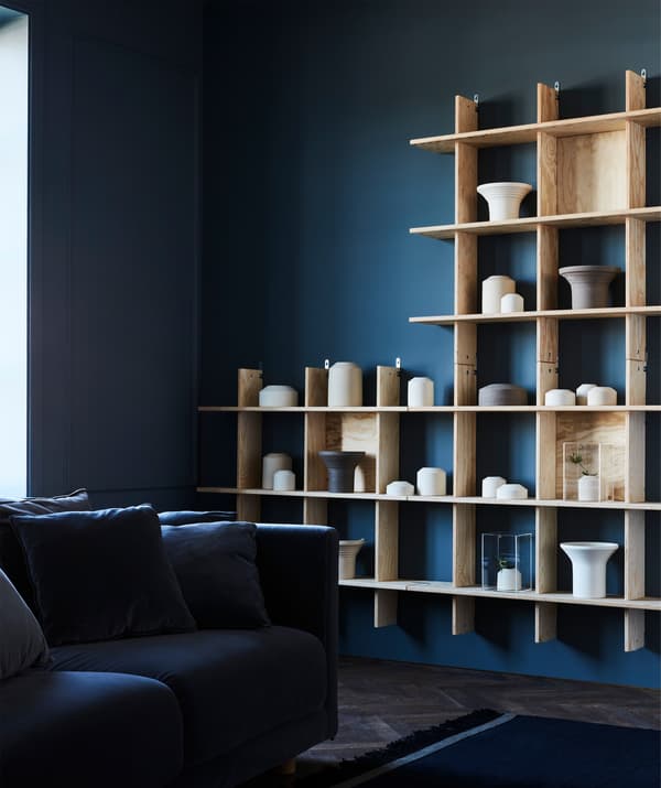 Una parete colore blu scuro con uno lo scaffale in legno chiaro INDUSTRIELL. Al suo interni, ci sono oggetti accuratamente selezionati come vasi, contenitori e altre suppellettili.
