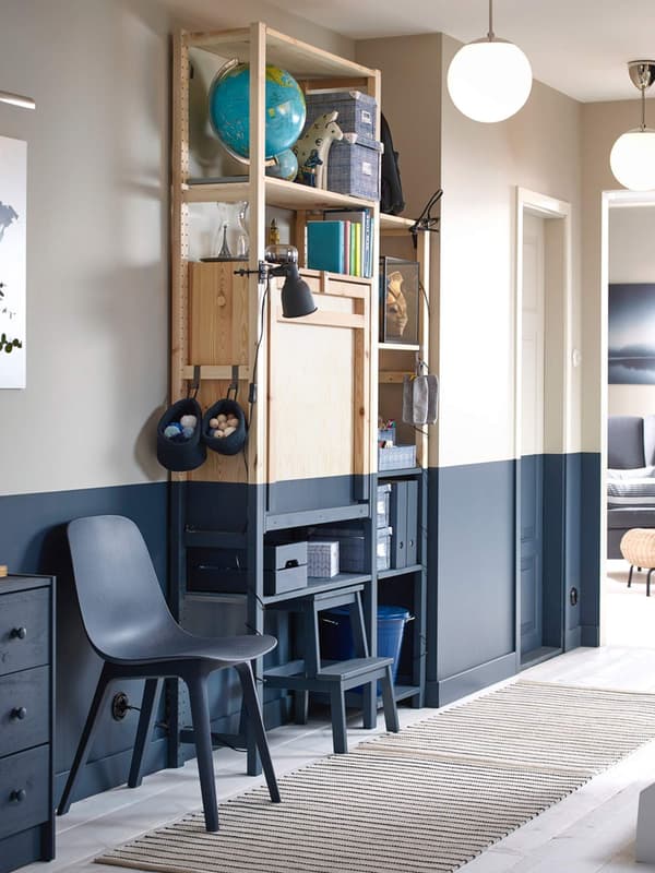 Una parete su cui sono appogiati due scaffali, una scaletta, una sedia e una cassettiera. Una parte è stata dipinta di blu come anche gli arredi. 