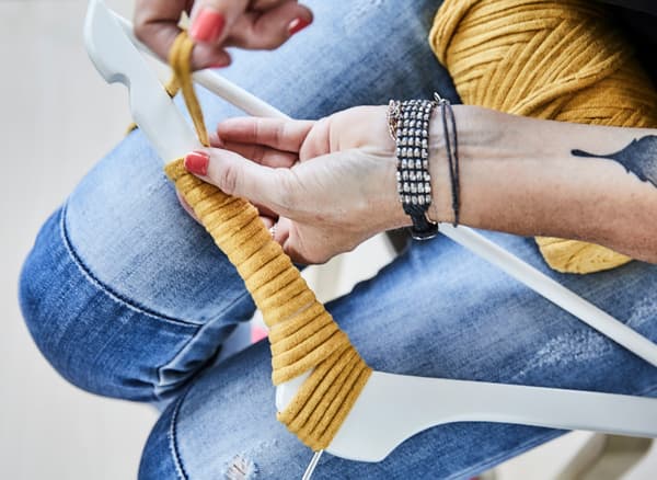 Una persona enrotllant una tira gruixuda de color groc en un penja-robes blanc BUMERANG per crear un element decoratiu únic.