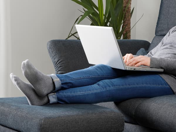 Una persona estirada en el sofá con un ordenador portátil
