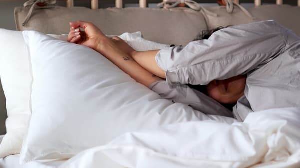 Una persona in pigiama è sdraiata su un letto BJÖRKSNÄS in betulla con biancheria da letto ÄNGSLILJA bianca - IKEA